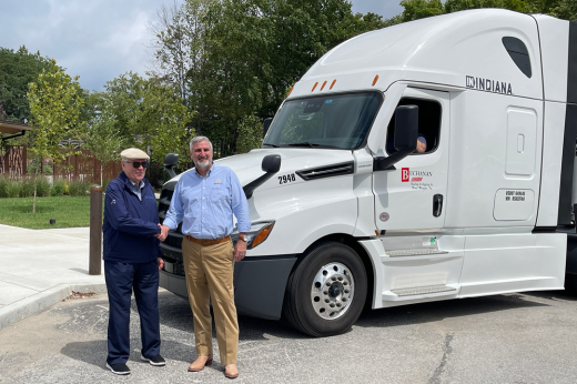 Owner Geary Buchanan and Indiana Governor Eric Holcomb shake hands next to a Buchanan Hauling and Rigging, Inc. truck with the "IN Indiana" campaign logo on it.