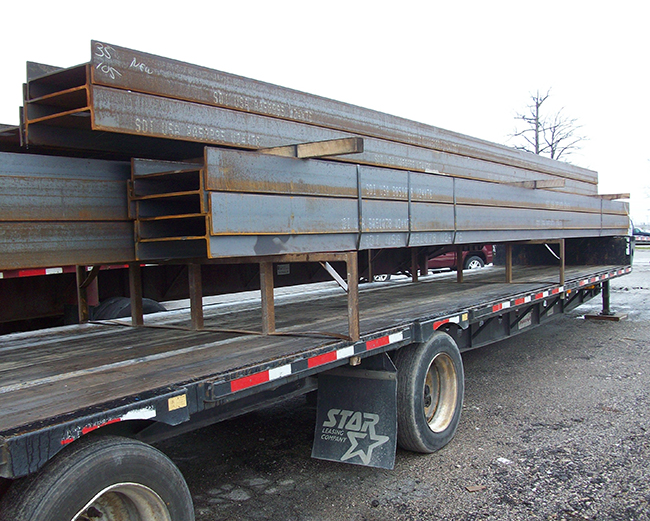 Flatbed truck transporting steel beams for construction project.