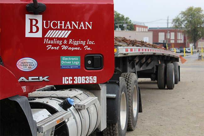 Open deck trucking transporting industrial freight on interstate highway.