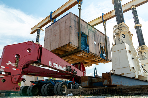 Industrial stamping press being positioned by crane for loading onto a heavy haul trailer