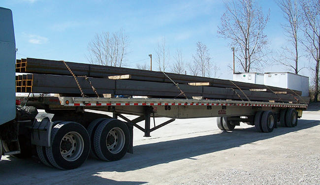 Flatbed truck transporting structural steel beams for infrastructure construction.