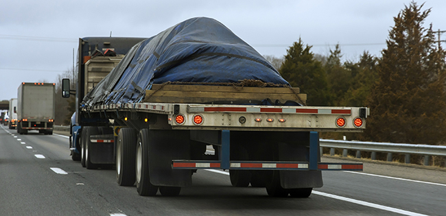 Open deck trucking hauling construction materials on interstate highway.