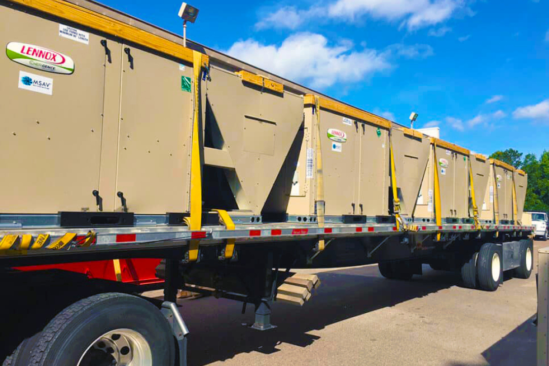 HVAC units ready to be unloaded at a jobsite on the back of a flatbed semi trailer and truck.