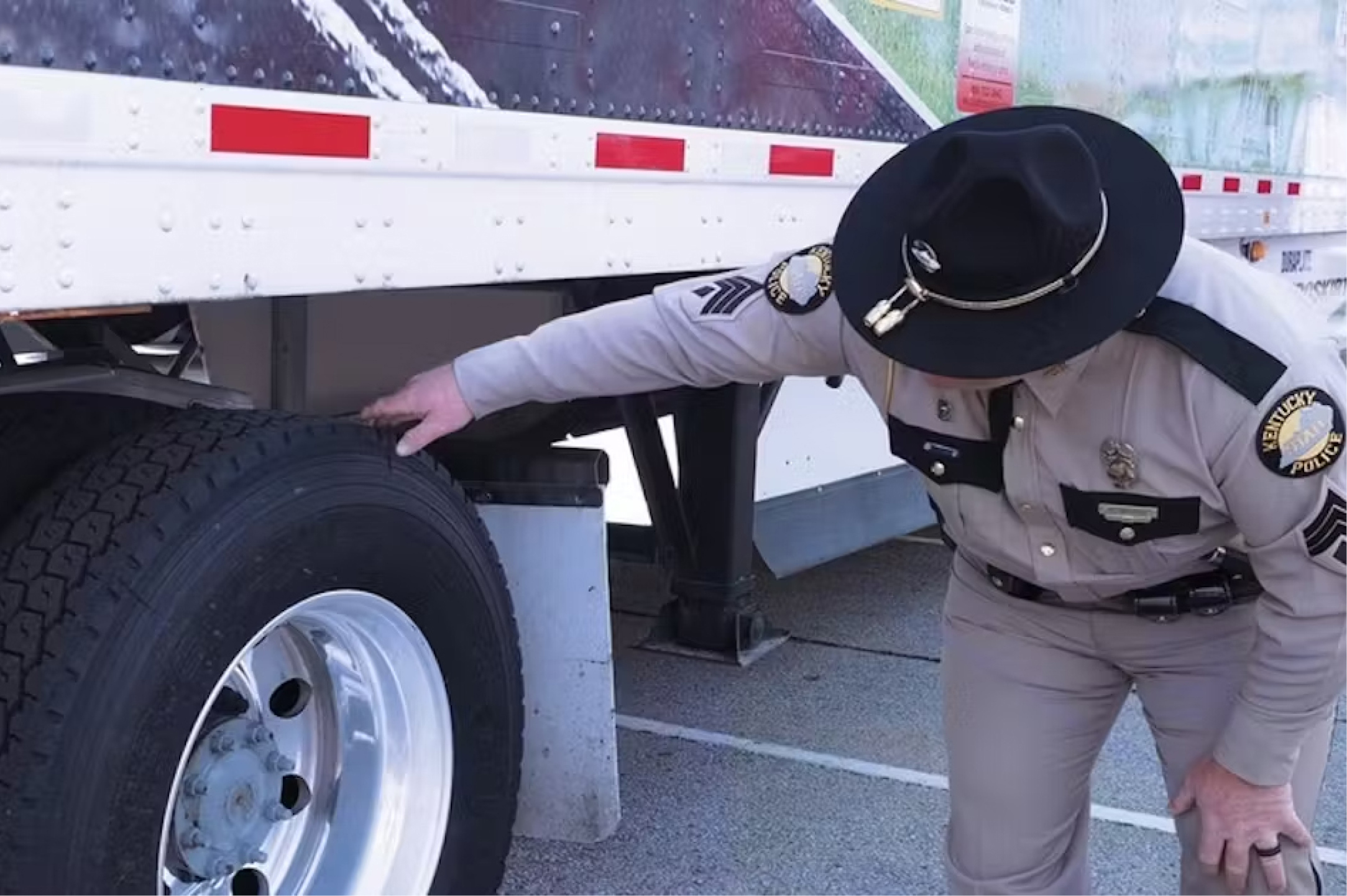 State patrol officer looks at the wear on a semi truck trailer at a roadside inspection.