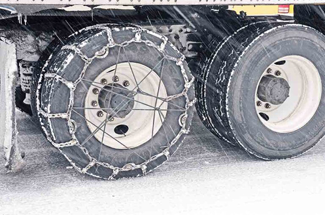 Semi truck trailer with tire chains on to handle icy weather conditions.