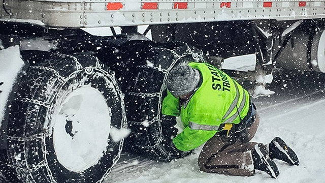State trooper inspects a semi truck driver's tire chains on a snowy road.