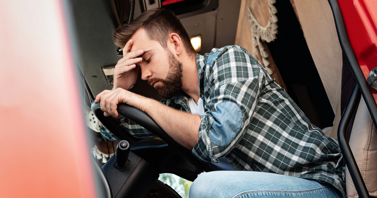 Truck driver with a headache slouched over his steering wheel truck cab